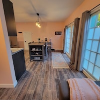 A modern kitchen with dark wooden flooring, a dining area with a table and chairs, and a large window with curtains.