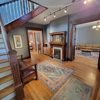 A spacious living area with a wooden staircase, a fireplace, and a large rug.