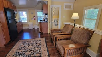 A spacious living area with a wooden sofa set, a patterned rug, and a kitchen in the background.
