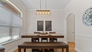 Een eetruimte met een houten tafel, banken en een kroonluchter. Er hangen twee borden in de lijst aan de muur en een decoratief element.