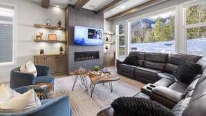 Een moderne woonkamer met een open haard, een grote televisie en uitzicht op een besneeuwde berg.