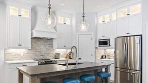 Een moderne keuken met witte kasten, een roestvrijstalen koelkast, een inbouwmagnetron en een centraal keukenblok met barstoelen.