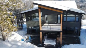 Een modern herenhuis met een groot balkon, omgeven door sneeuw en bomen.