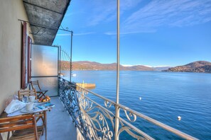 Un balcon avec une table préparée pour le petit-déjeuner, donnant sur un lac paisible, avec des montagnes qui se dessinent à l’horizon.
