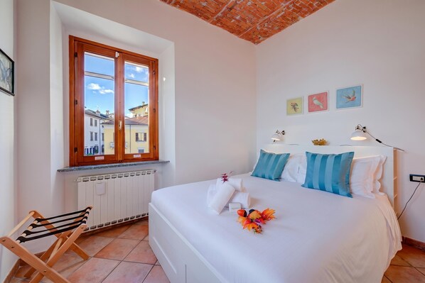 Une chambre d’hôtel avec un grand lit, une fenêtre donnant sur un beau paysage, un radiateur, une chaise en bois et un mur orné de trois tableaux.