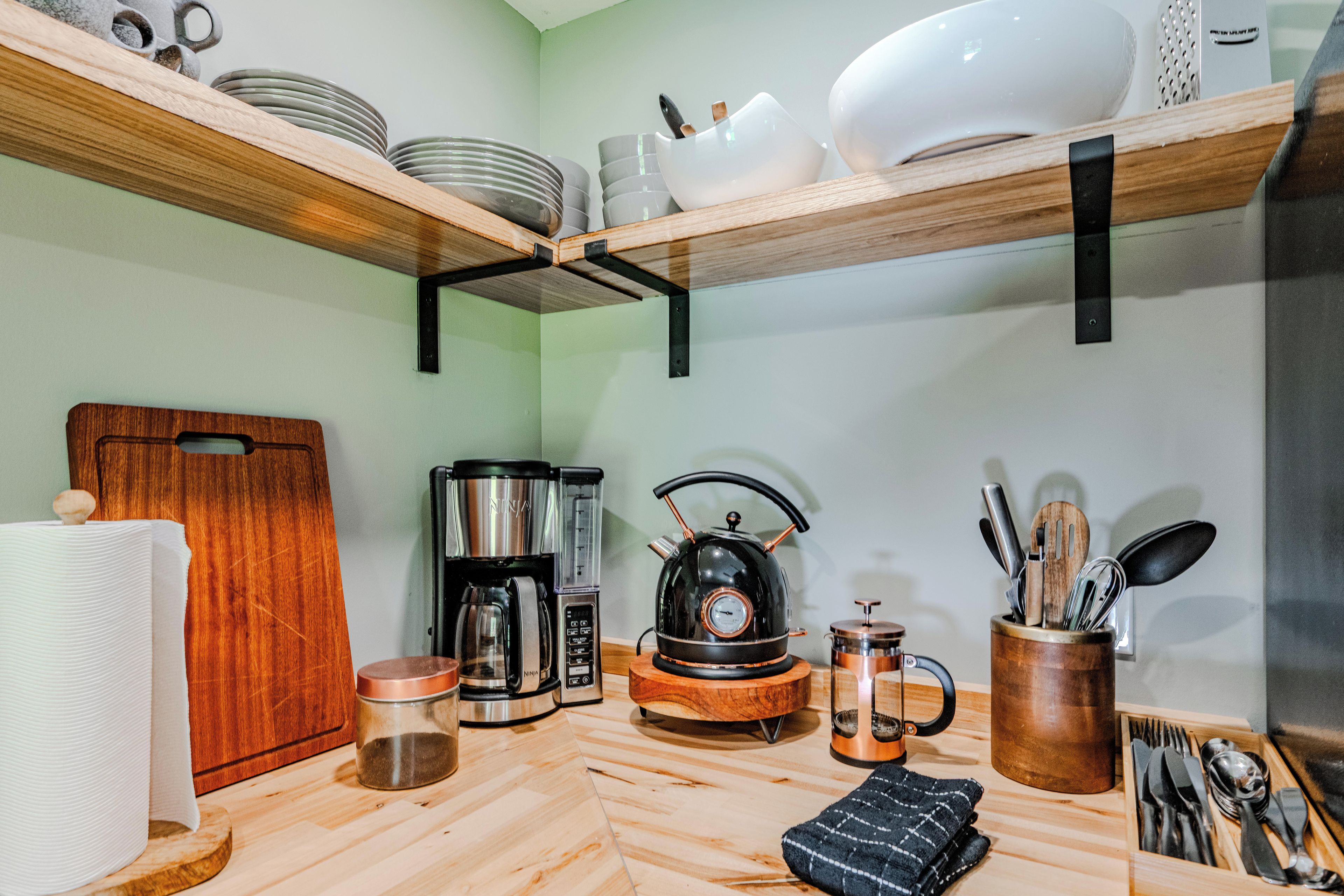 A kitchen with wooden shelves, a coffee maker, a kettle, and utensils.