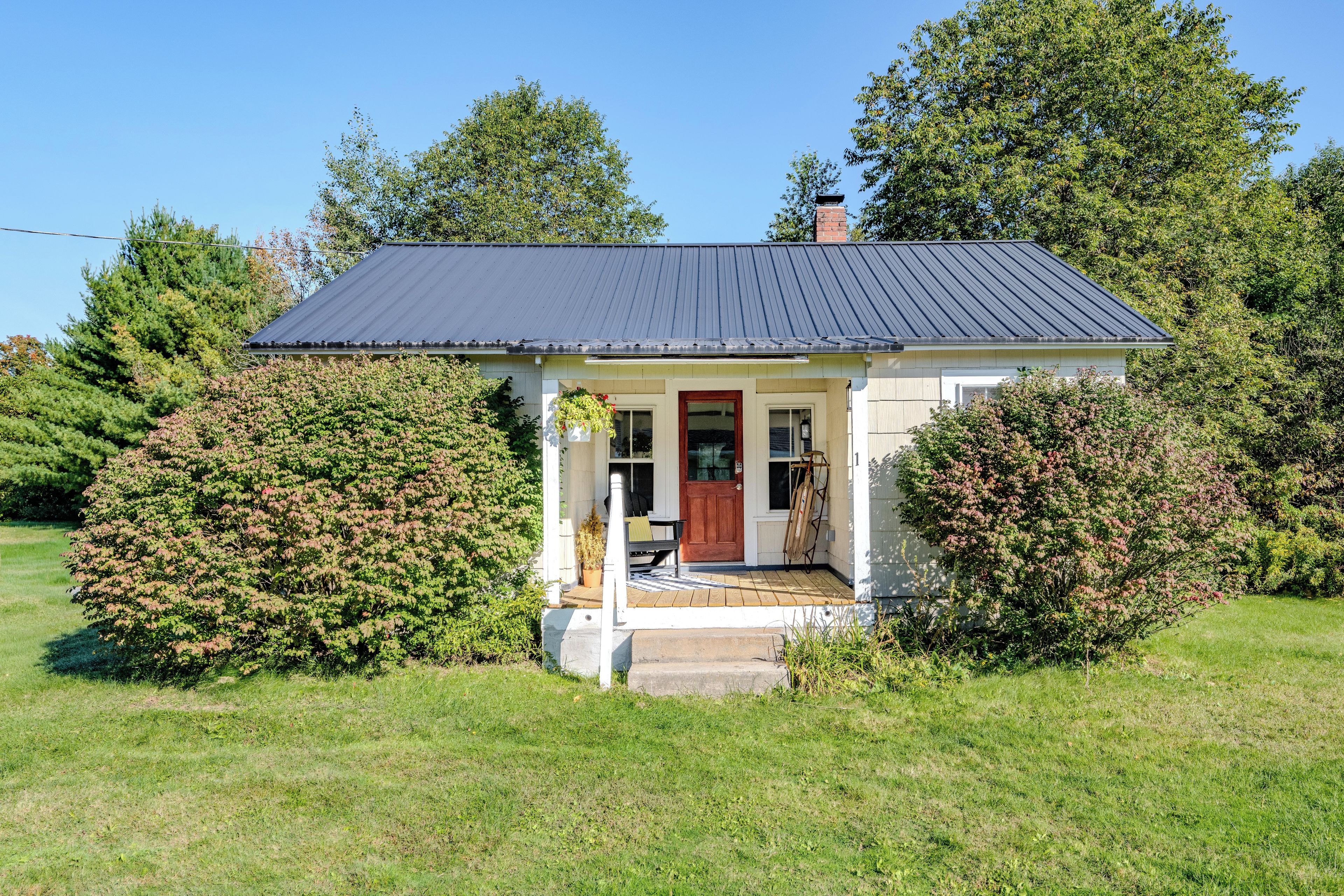 A small house with a dark roof, a front porch, and a red door.