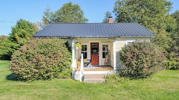 A small house with a dark roof, a front porch, and a red door.