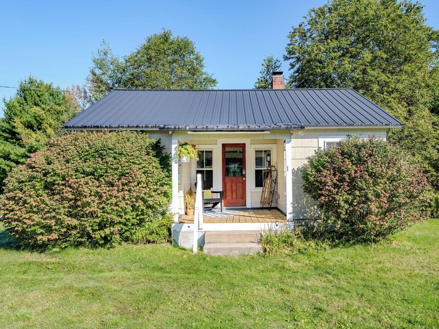 A small house with a dark roof, a front porch, and a red door.