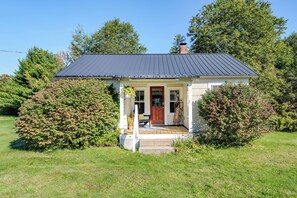 Ein kleines Haus mit dunklem Dach, einer Veranda und einer roten Tür.