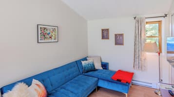 A living room with a blue sofa, two framed pictures, a window with curtains, and a lamp.