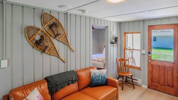 Una habitación con un sofá de cuero marrón, una silla de madera, una puerta con vistas y dos objetos fijados a la pared.
