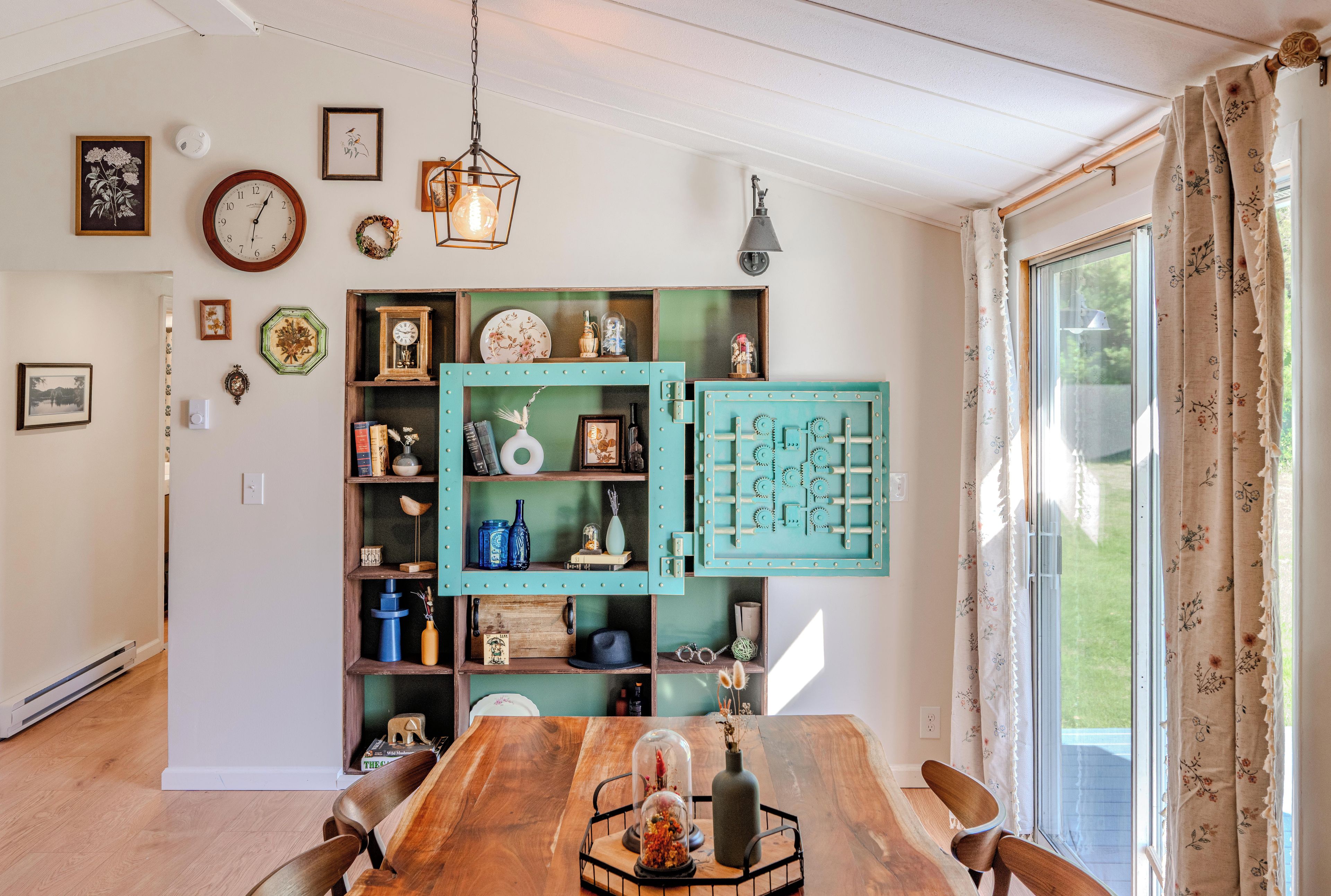 Un coin repas comprenant une table en bois, des chaises et une étagère ouverte de couleur turquoise, agrémentée de divers objets décoratifs.