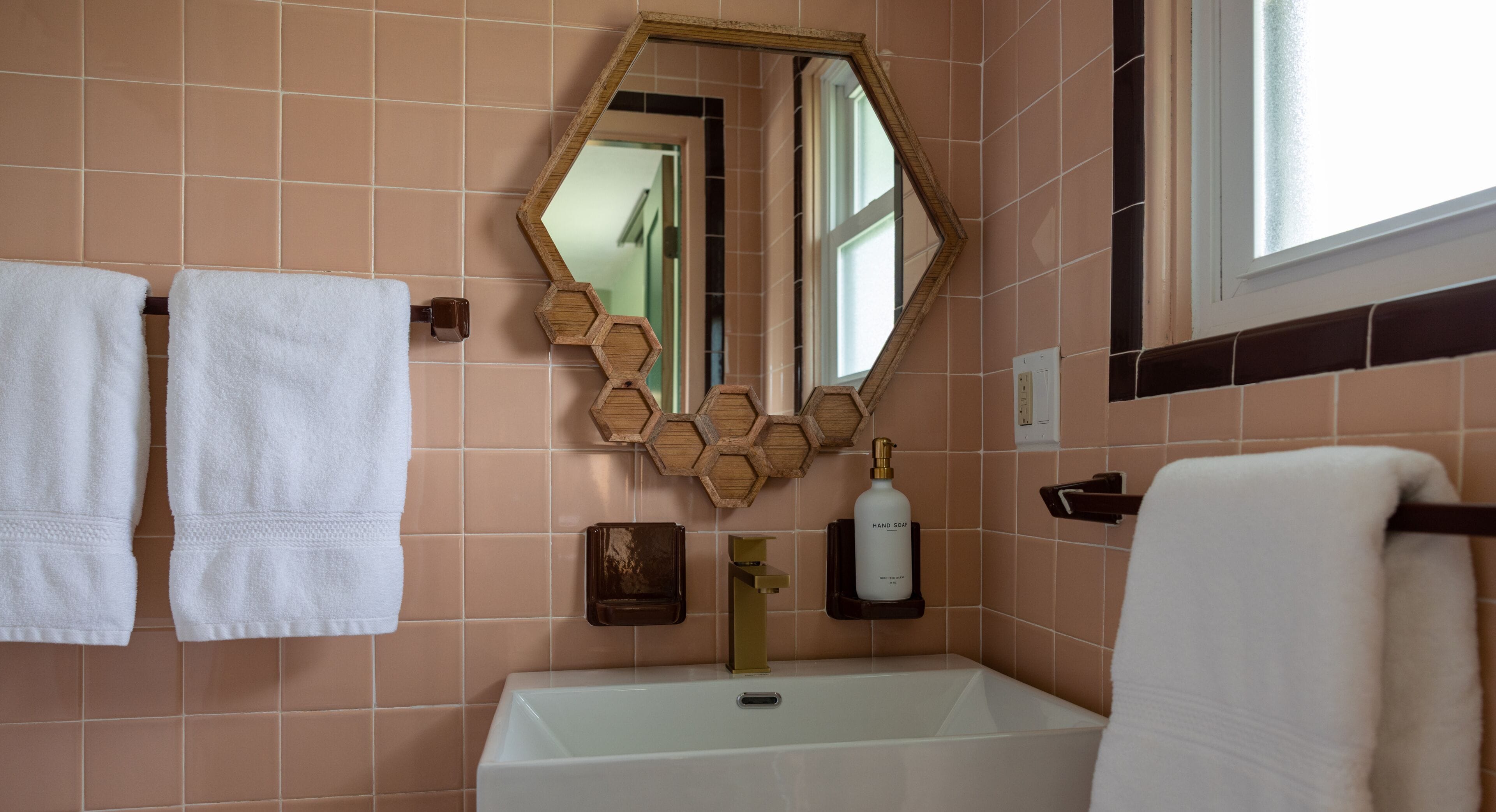 A bathroom with a white bathtub, a wooden hexagonal mirror, and two white towels hanging on the wall.