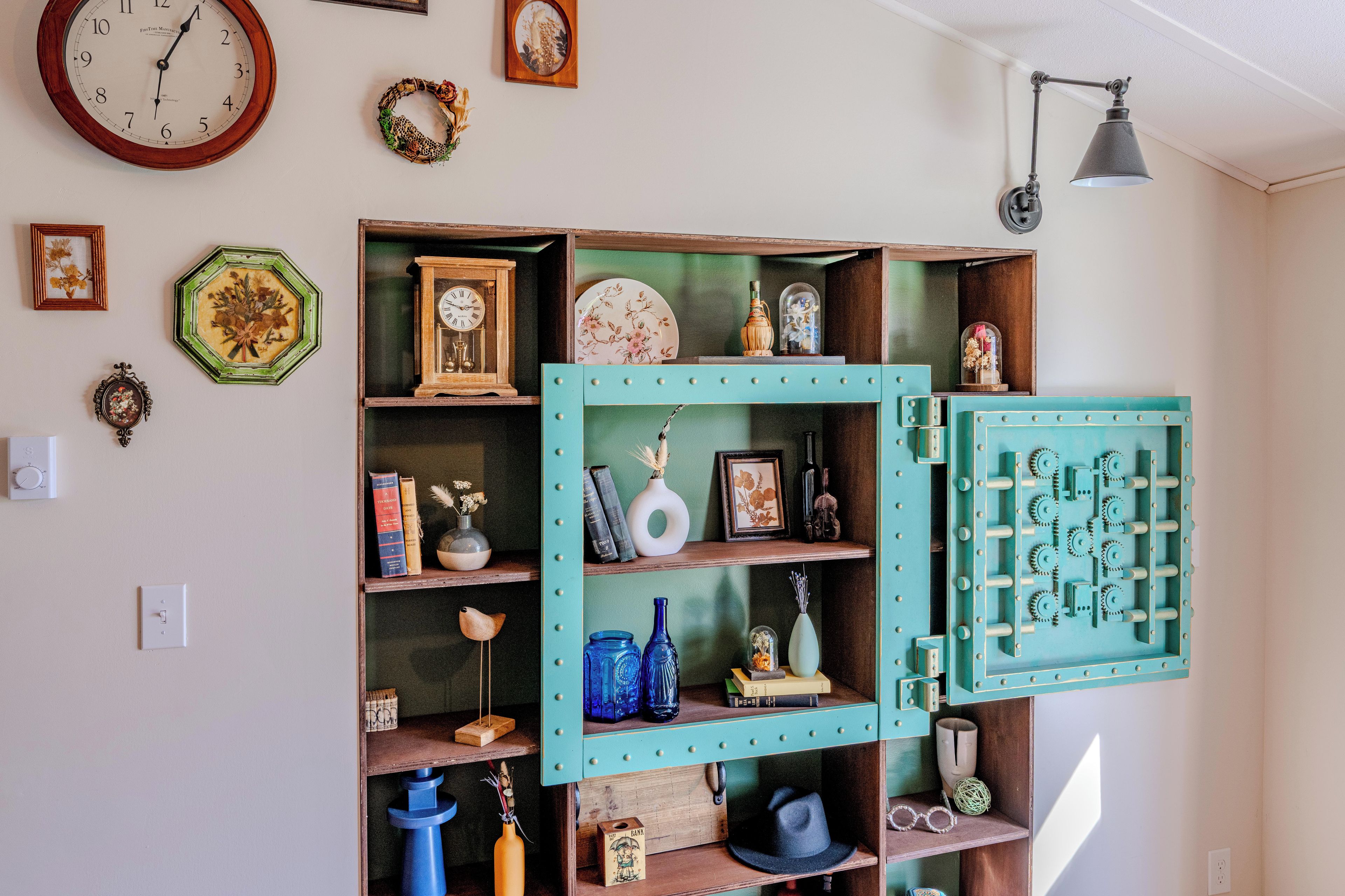A room with a wall clock, a framed picture, and a shelf with various decorative items.