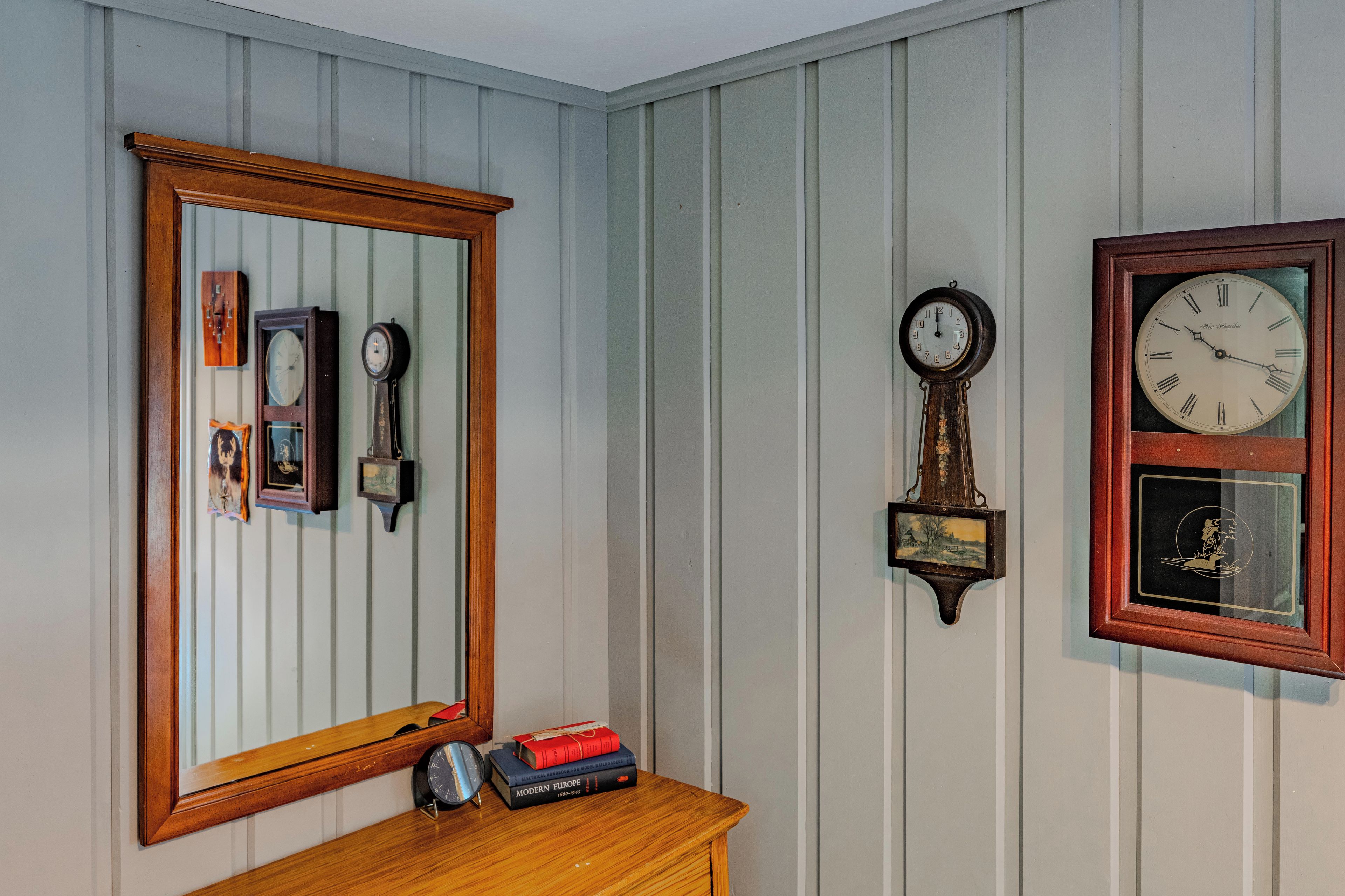 A room with a wooden dresser, a mirror, and a wall clock.