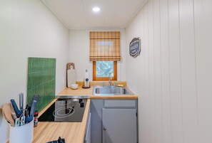 Une cuisine compacte comprenant un évier, une fenêtre avec stores, un petit réfrigérateur et un crédence de couleur verte.