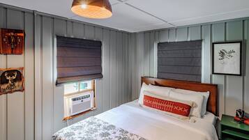 Un dormitorio con cama, una ventana con persianas, un reloj de pared e impresión enmarcadas de motivos botánicos.