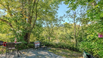 An outdoor seating area with tables and chairs, surrounded by dense foliage and trees.