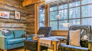 Interior acogedor de una cabaña de madera con un sofá azul, sillones estampados y una mesa de madera.