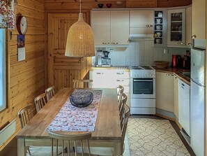 Un interior de madera con una mesa de comedor, sillas, una cafetera, una estufa y armarios.