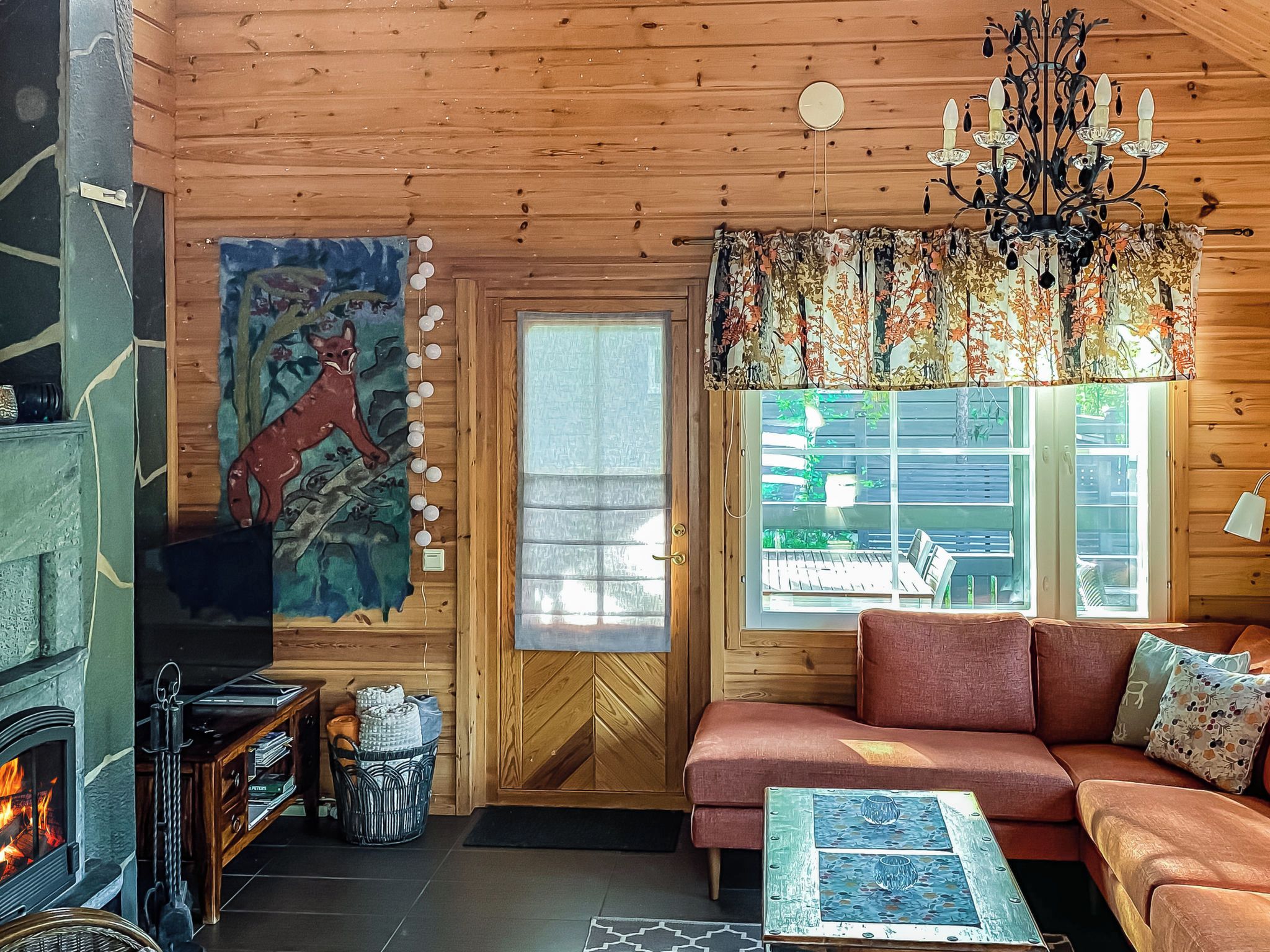 Een gezellig chaletinterieur met een open haard, een bank, een gestreepte plaid en een groot raam.