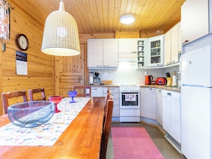 A cozy kitchen with wooden walls, a dining table with chairs, a hanging light fixture, and modern appliances. - Tulikettu 1 by Interhome (Pelkosenniemi)