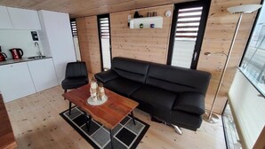 Ett kompakt vardagsrum med ett litet kök, en svart soffa, ett träbord och ett stort fönster.