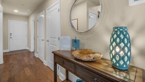 A hallway with wooden flooring, white doors, a wooden console table with a decorative bowl and a blue vase, and a wall-mounted mirror. - Beach Access Condo with Pool and Hot Tub (Miramar Beach)