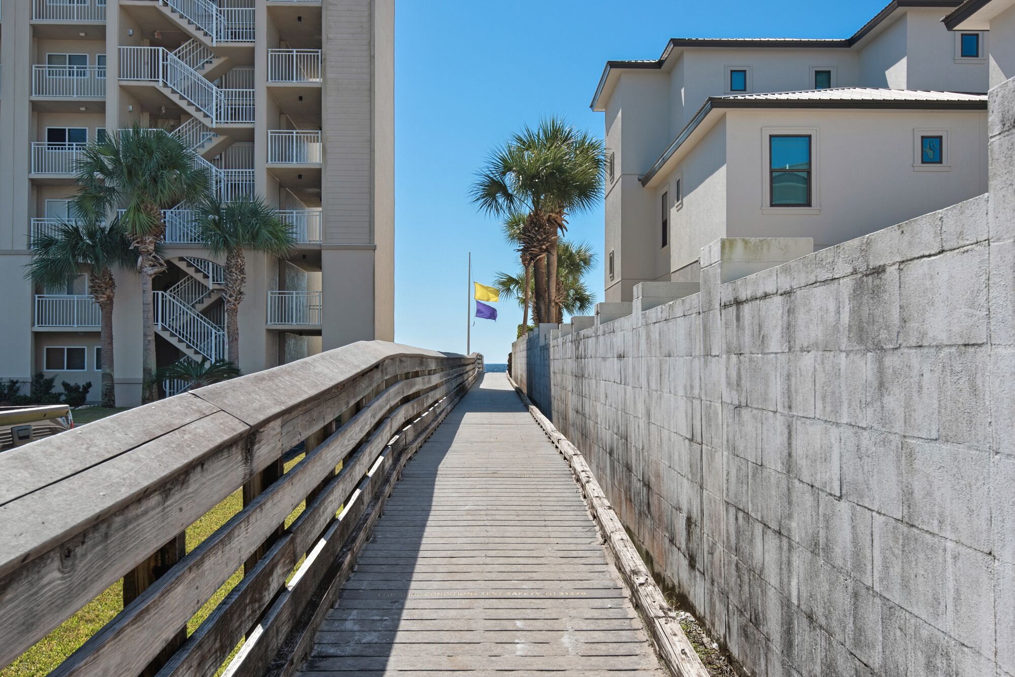 A wooden boardwalk leading to a building with a concrete wall and a flag.