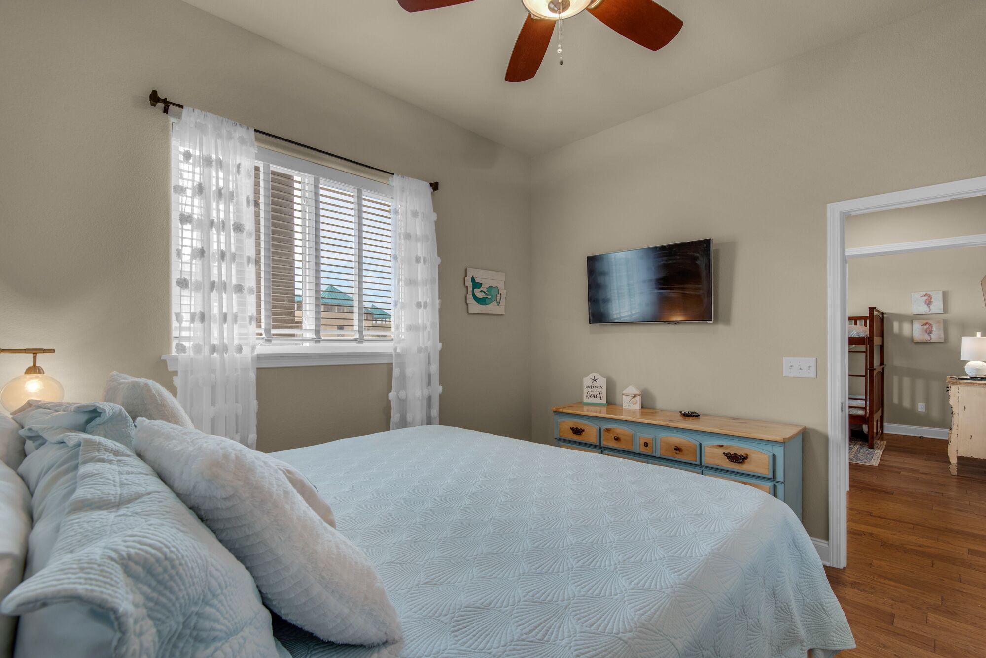 Un dormitorio con cama, cómoda, ventilador de techo, ventana con persianas y televisor en la pared.