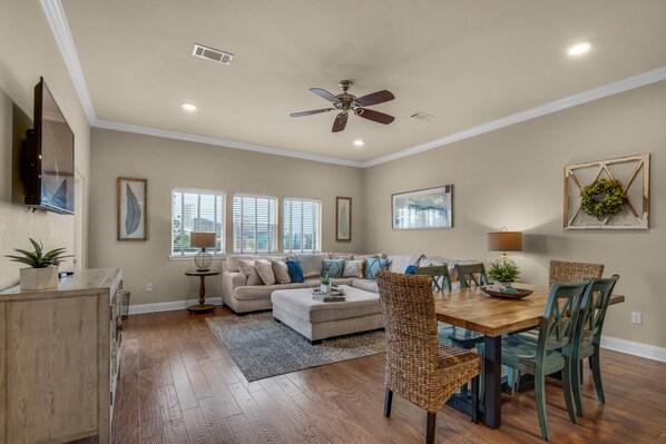 A spacious living room with a large sofa, a dining table with chairs, and a ceiling fan.