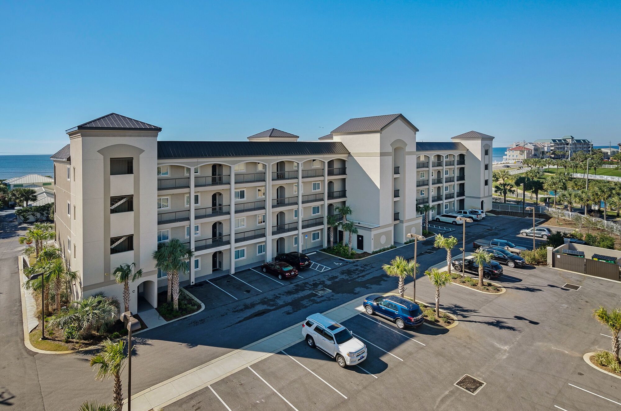 A multi-story hotel with a central courtyard, parking lot, and a view of the ocean.