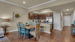 A spacious kitchen with wooden cabinets, a central island, and a dining area with blue chairs. - Beach Access Condo with Pool and Hot Tub (Miramar Beach)