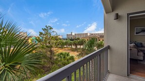 A balcony with a view of a landscaped area, including palm trees and a building in the background. - Beach Access Condo with Pool and Hot Tub (Miramar Beach)