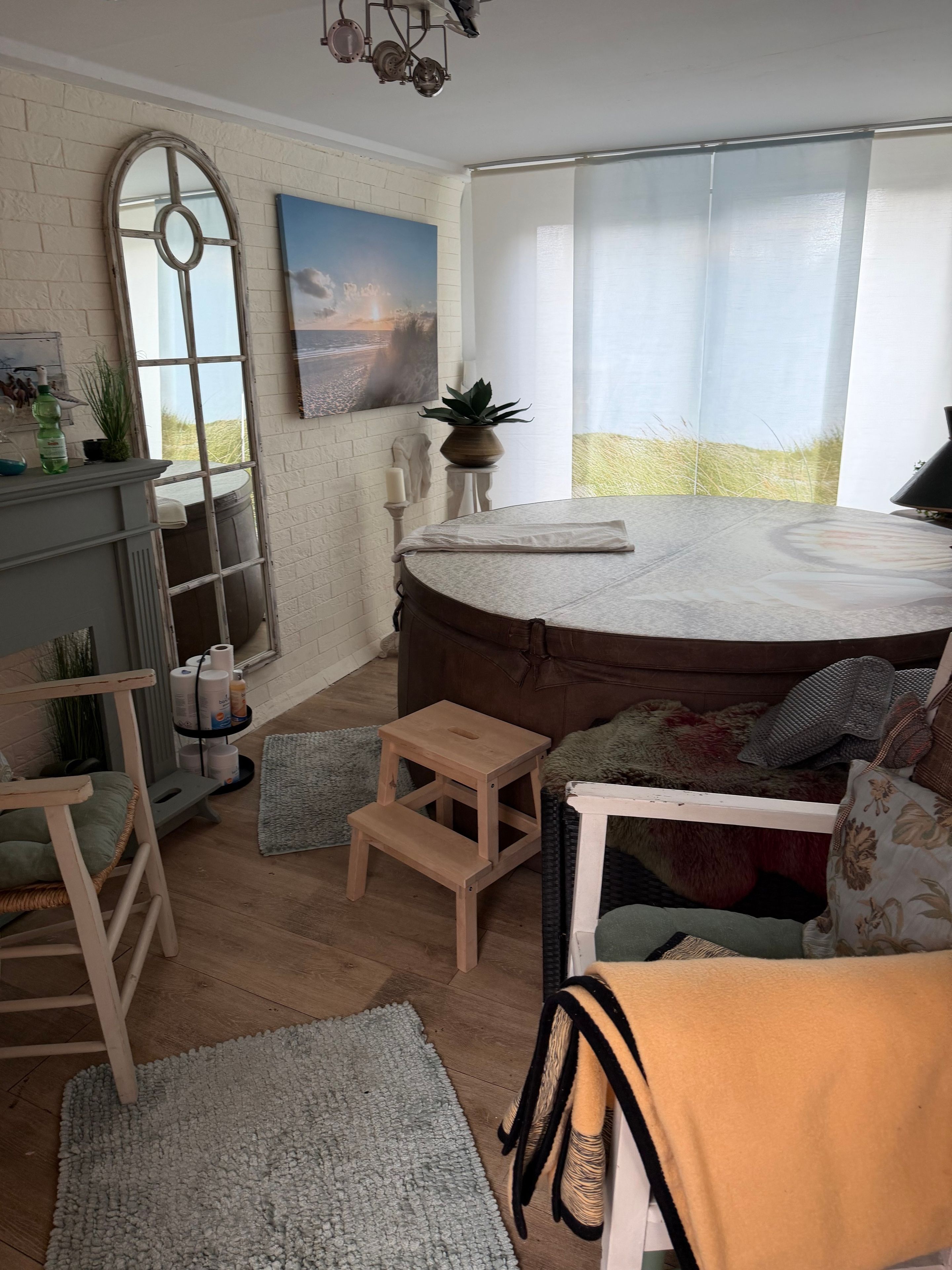 A cozy living room with a round bed, a wooden stool, a cushioned chair, and a small table.