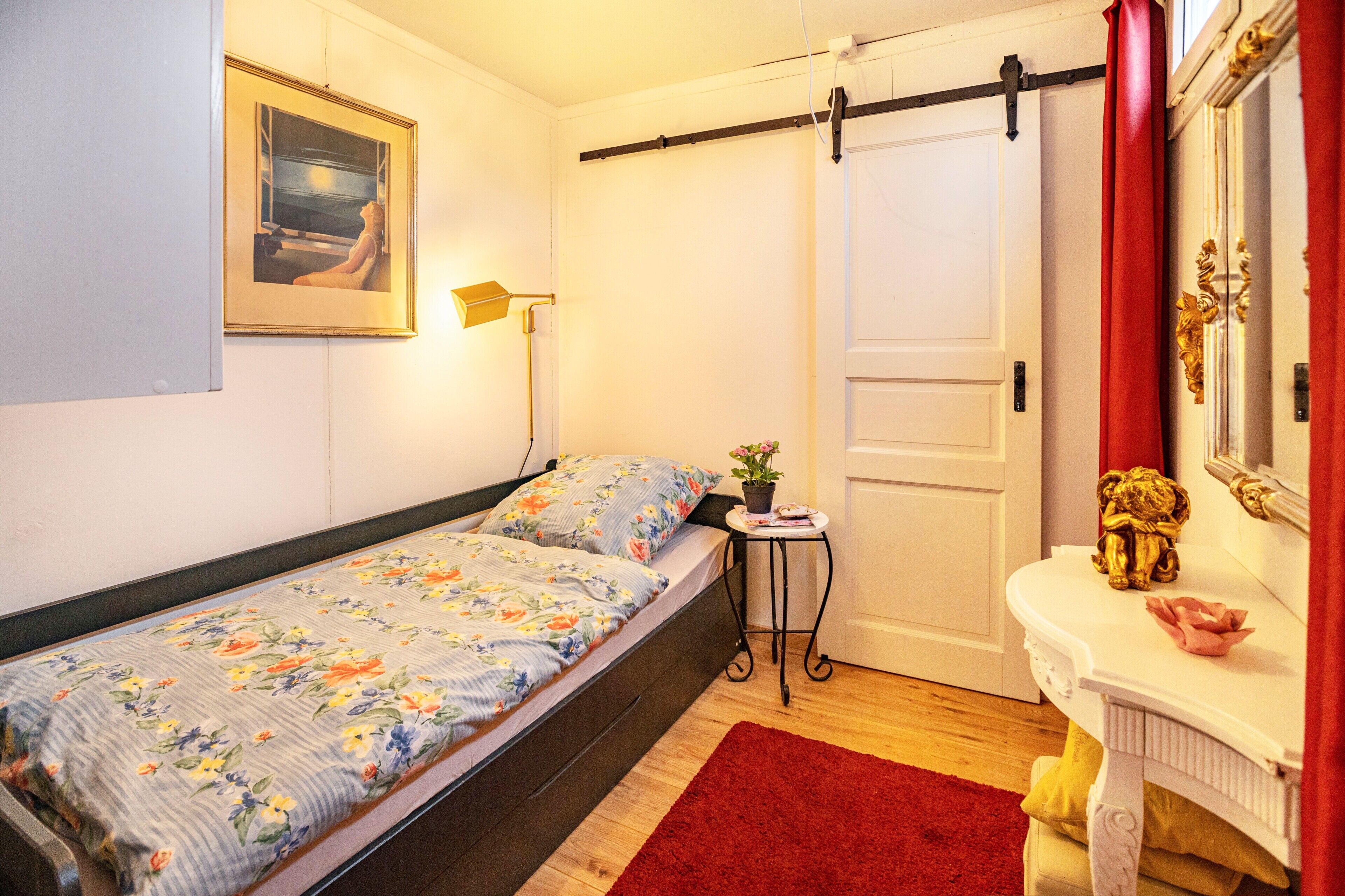 Et soveværelse med en seng, et lille bord med en plante, et spejl og en dør med gardin.
