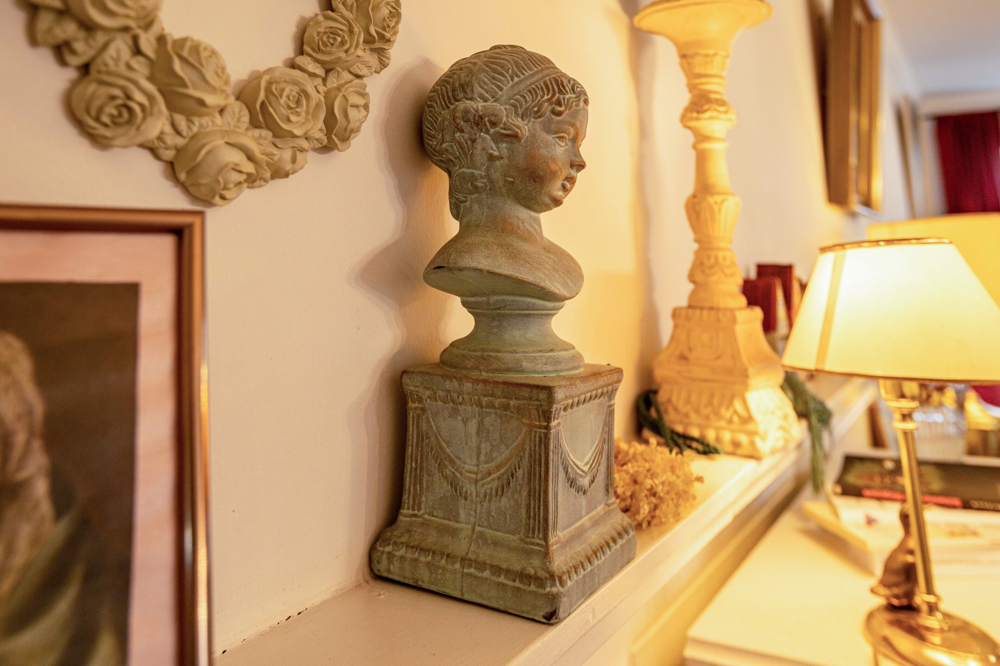 Une sculpture en buste posée sur un piédestal, une lampe et un tableau encadré sur la cheminée.