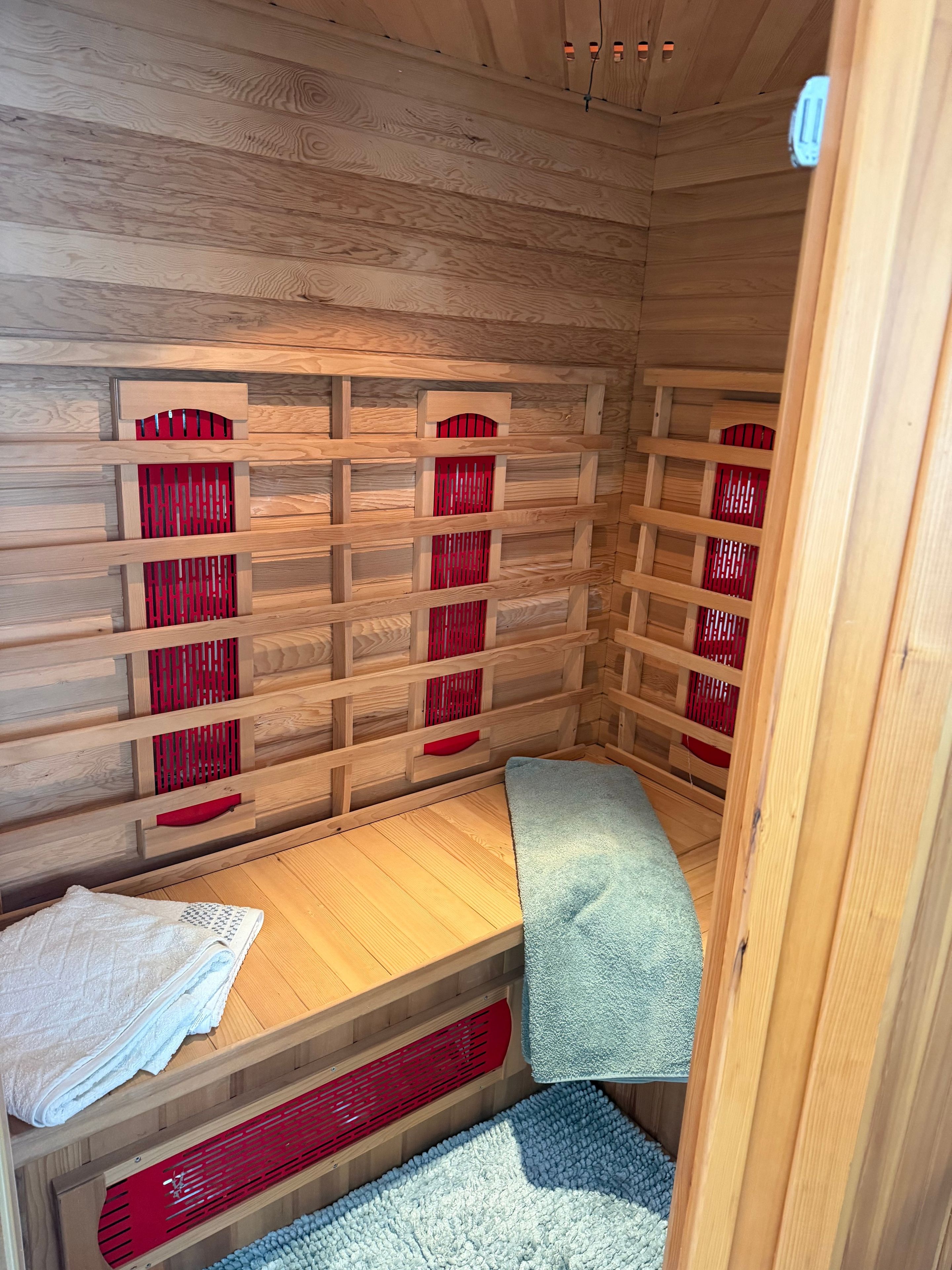 Ein Zimmer aus Holz mit einem Bett, einer Bank und einer Wand mit roten Lamellen.