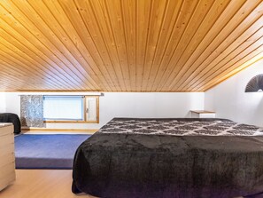 A room with a sloped ceiling, a bed with a patterned bedspread, a window with a view, and a wall-mounted fan.