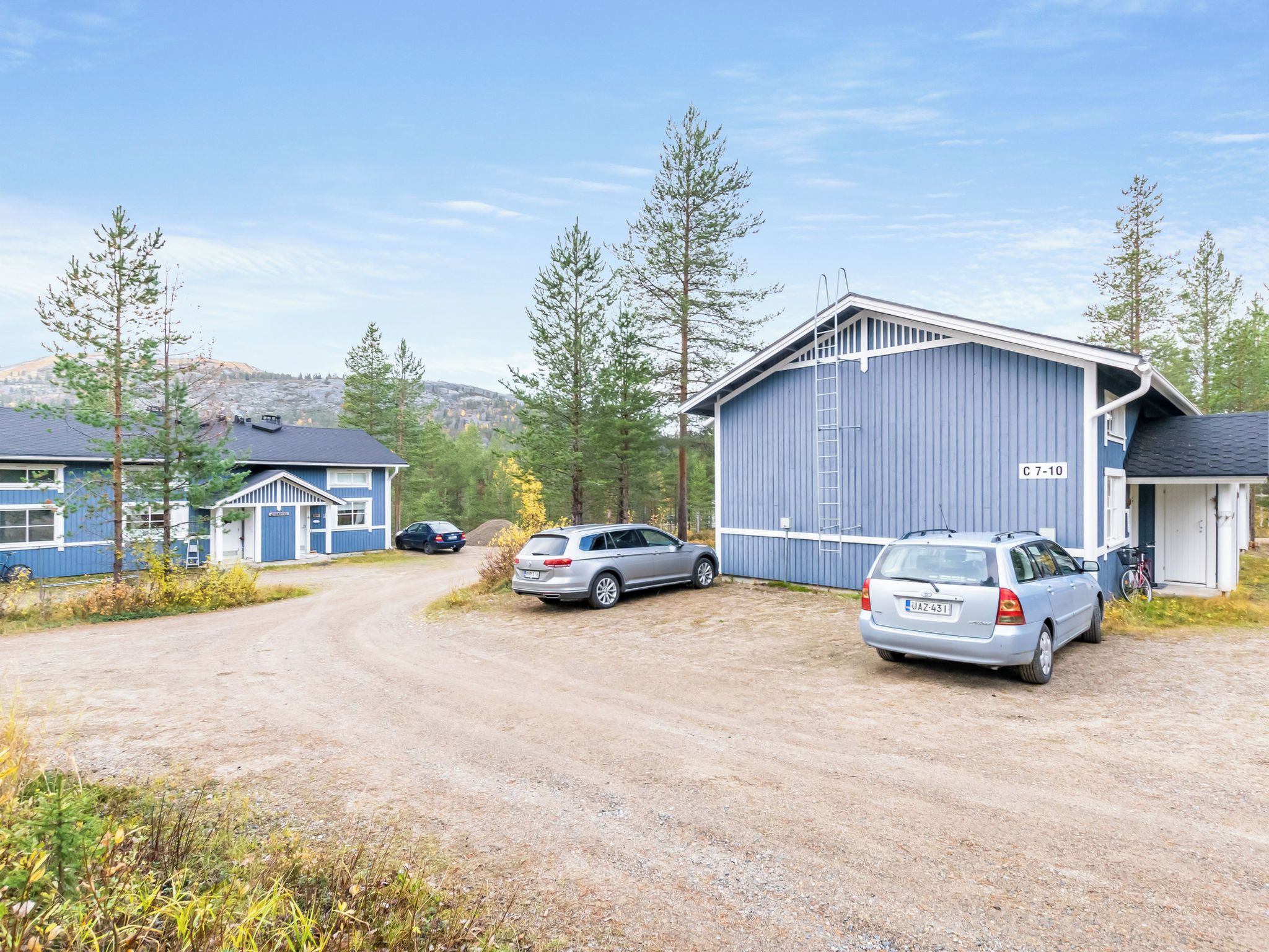 A gravel driveway leading to a blue building with a car parked in front.
