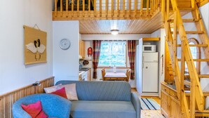 Una sala de estar acogedora con un sofá gris, un sillón azul y una escalera de madera que sube a un nivel superior.