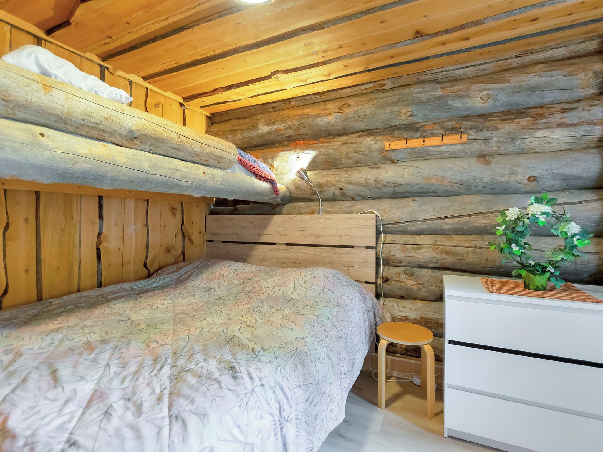 A bunk bed with a patterned bedspread, a bedside table with a lamp, and a small stool.