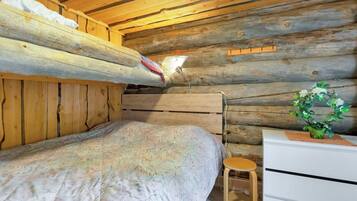 A bunk bed with a patterned bedspread, a bedside table with a lamp, and a small stool.