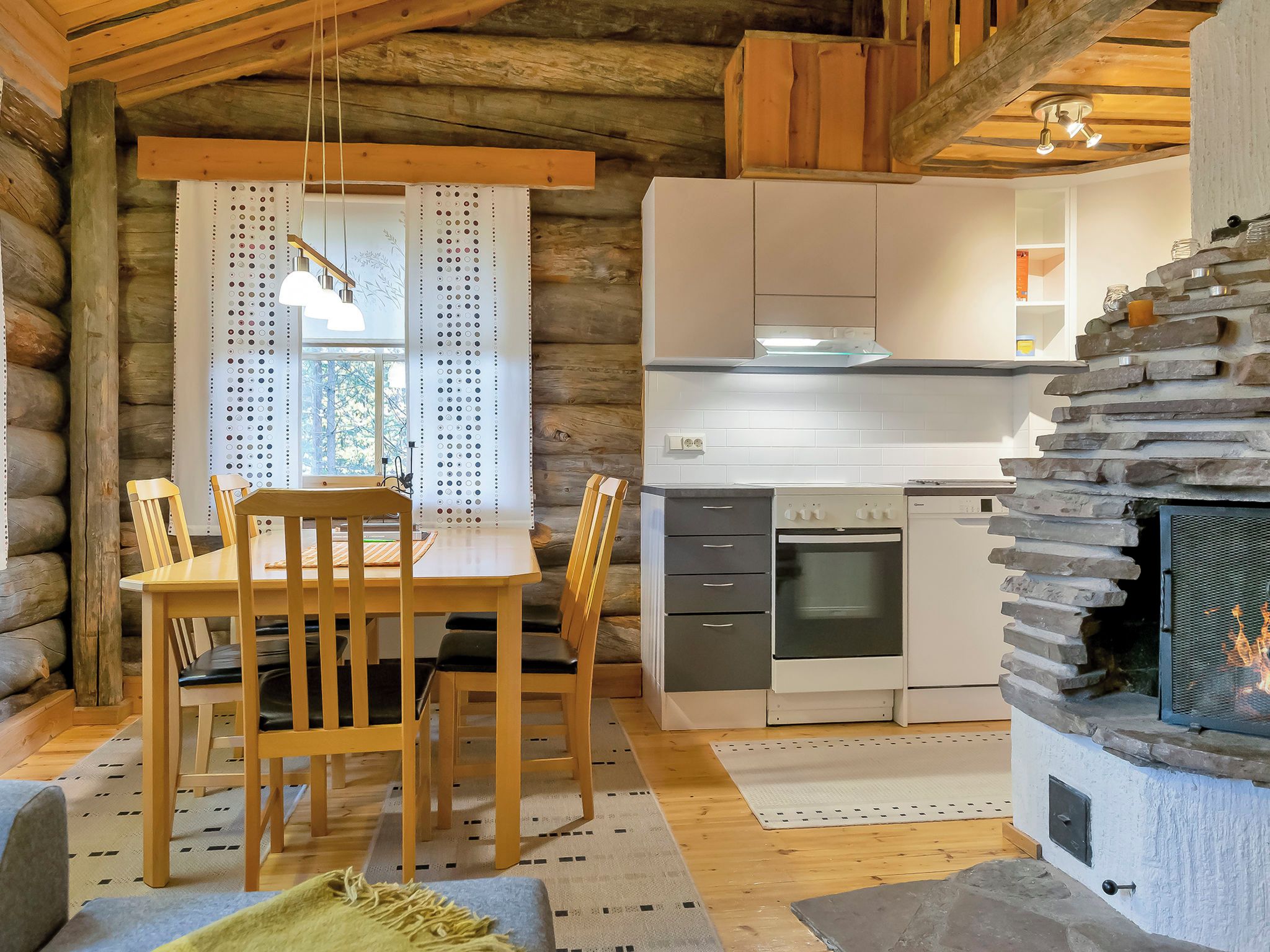 A log cabin interior with a dining area, kitchen, and fireplace.