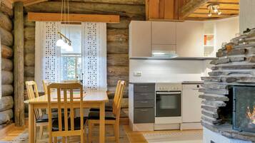 A log cabin interior with a dining area, kitchen, and fireplace.
