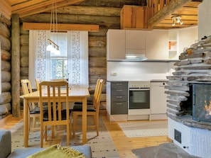 Interior de una cabaña de troncos con comedor, cocina y chimenea.