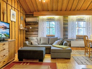 A cozy cabin interior with a sofa, ottoman, wooden cabinets, a television, and a window with curtains. - Luppokero 1 by Interhome (Pelkosenniemi)
