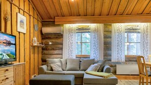 L’intérieur d’un chalet confortable, avec un canapé, un pouf, un plancher en bois et un téléviseur posé sur un meuble.