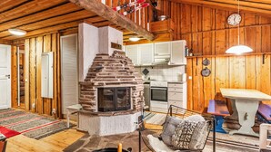 Ein rustikales Blockhaus mit Kamin aus Stein, Holzwänden, einer Küchenzeile und einem Esstisch.